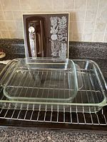 Photo showing two glass baking dishes front: smaller 8x8 inch and larger 9x13 inch, with decorative cookie sheet vertically placed behind them on counter