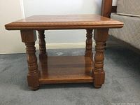 Front view of the solid wood side table showing four turned legs and a bottom shelf with a crack.
