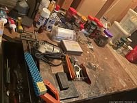 Workbench surface showing various small containers of screws, bolts, jars, clamps, and saw handles