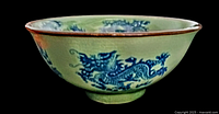 Side angled view of antique celadon bowl showing blue dragon motif and brown trim on rim.