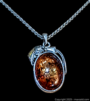 Close-up of the oval Baltic amber colour pendant with silver-tone decorative setting on a black background.
