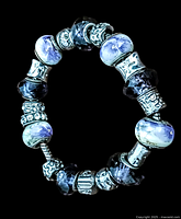 Top view of the bracelet showing porcelain beads with purple floral motif and faceted dark art glass beads separated by silver-tone textured spacers.