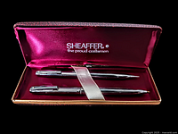 Set of two Sheaffer Stylist pens displayed in original burgundy satin-lined case with 'Sheaffer the proud craftsmen' logo on lid.