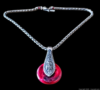 Full view of the silver chain necklace with round pink agate pendant featuring black inclusions and ornate silver bail against black background.