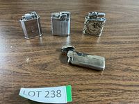 Four vintage silver-tone metal lighters arranged on wooden surface showing various finishes and designs.