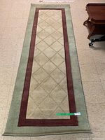 Full view of the rectangular carpet runner showing beige diamond quilting pattern with dark red and light green borders.