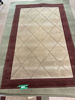 Full view of the rectangular area carpet showing the central beige section with diamond pattern and brown and green borders.