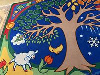 Close-up showing part of the carpet with a large tree with green leaves, a yellow bird, a white sheep, and a red tulip flower on a blue background.