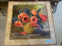 Card table with a floral painting of red poppies and purple flowers in a yellow vase on the top surface, showing the full tabletop and part of the floor.