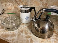 All three items: Glass tea pot, Corning Ware coffee pot with blue cornflower, and silver metal kettle with black handle.