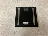 Electronic bathroom scale with light reflections, Graviti brand label, sticker with lot number on top center.