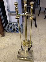 Brass fireplace tool set with stand on linoleum floor, showing entire set.