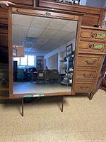 Full front view of large mirror with wooden frame and right side storage drawers with brass handles.