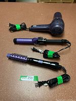 YOU brand hair dryer, purple and black curling iron, and Conair heated styling brush arranged on table with cords tied.