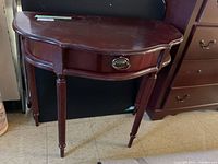 Half moon-shaped wooden side table showing front with drawer and four legs.
