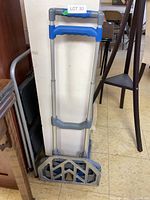 Front view of folding moving dolly showing metal frame, blue plastic handles, and baseplate folded up.