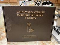 Photo of the closed whiskey decanter set box showing the product name and contents in gold text on brown background.