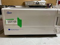 Side view of off-white Oster wide slot toaster with logo and broad slot for bread, labeled LOT 68.