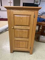 Front view of pine pantry cabinet showing single door with knob and raised panels.