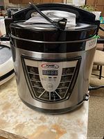 Front and top view of the Rival Power Pressure Cooker XL showing the digital control panel and cord wrapped on top.