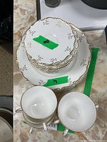 Stack of dinner plates and saucers with two cups on top, showing the gold detail and design on edges.