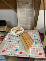 Full view of Scrabble board set up with the tile racks, bag of tiles on board, and framed dictionary/instruction sheet behind