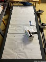 Top view of the white padded adjustable bed frame surface and black fabric border with remote and some assembly hardware on it.