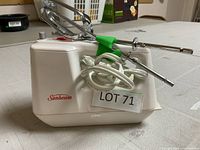 Side view of white Sunbeam hand mixer with power cord and attachments.