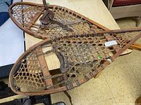 Pair of vintage wooden snowshoes placed on a table, showing front and side views.
