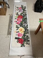 Large vertical floral scroll wall hanging with peonies in pink, red, and yellow with green leaves on a fabric scroll with wooden rods.