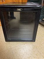 Front view of black Danby wine fridge with glass door, showing the whole fridge and floor.