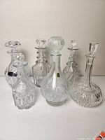 Front view of all six clear glass and crystal decanters arranged on a flat surface, showcasing varied shapes and decorative patterns.