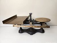 Side view of the antique balance scale showing the cast iron body, brass trays and ruler scale.