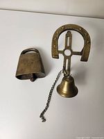 Photo showing the two brass bells on a white background, one rectangular with a handle, the other mounted on a horseshoe-shaped frame with a chain.