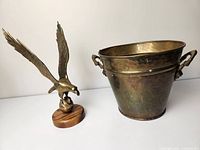 Wide shot of brass eagle statue and brass bucket side by side on white surface