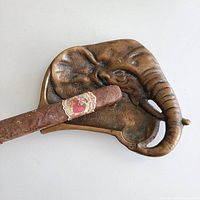Top view of antique bronze elephant head ashtray with cigar resting on it, showing detailed textured elephant features.