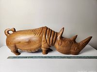 Side view of the carved wooden rhino with ruler for scale, showing detailed carving and smooth finish.