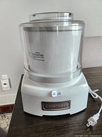 Front view of Cuisinart ice cream maker showing white base with control buttons and transparent mixing bowl on top.