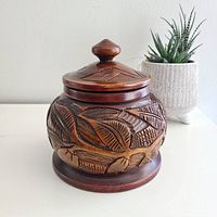 Front side view of the carved wooden bowl vase with lid, showing detailed leaf carvings and overall shape.