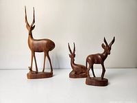 Three hand carved wooden antelope figurines of different sizes and poses displayed together on a white surface