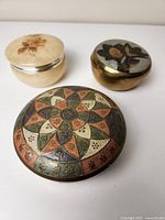 Top view of 3 small round trinket boxes showing alabaster and two enameled brass designs.