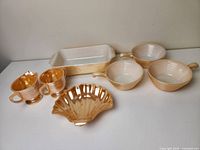 Peach lusterware Fire King dishes and cookware including two handled cups, shell dish, rectangular baking dish, and three cooking pots.