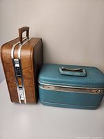 Brown Samsonite travel train case and blue portable bar case side by side on a flat surface showing exterior from the front and side view
