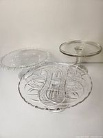 Three glass cake stands shown together on a white background, including a clear glass pedestal stand, a beaded edge tray, and an etched large tray.