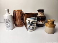 Five pottery and vase items arranged side by side on a white surface with plain background.