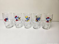 Front view of all five Smurfs glasses in a row showing various character illustrations.