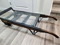 Side perspective showing wooden handles, glass top secured with metal frame, and part of the wheels under the cart.