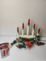 Vintage electric Yule log candelabra with five candle bulbs and attached greenery with poinsettia flowers, shown unlit alongside two packages of replacement bulbs