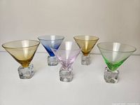 Front view of five vintage cocktail glasses in pastel colors with cube-shaped clear glass bases.