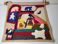 Full view of wool fabric wall hanging with Native animal and human figure motifs, colors predominantly cream, red, blue, yellow, and brown, mounted on wooden rod with cord for hanging.